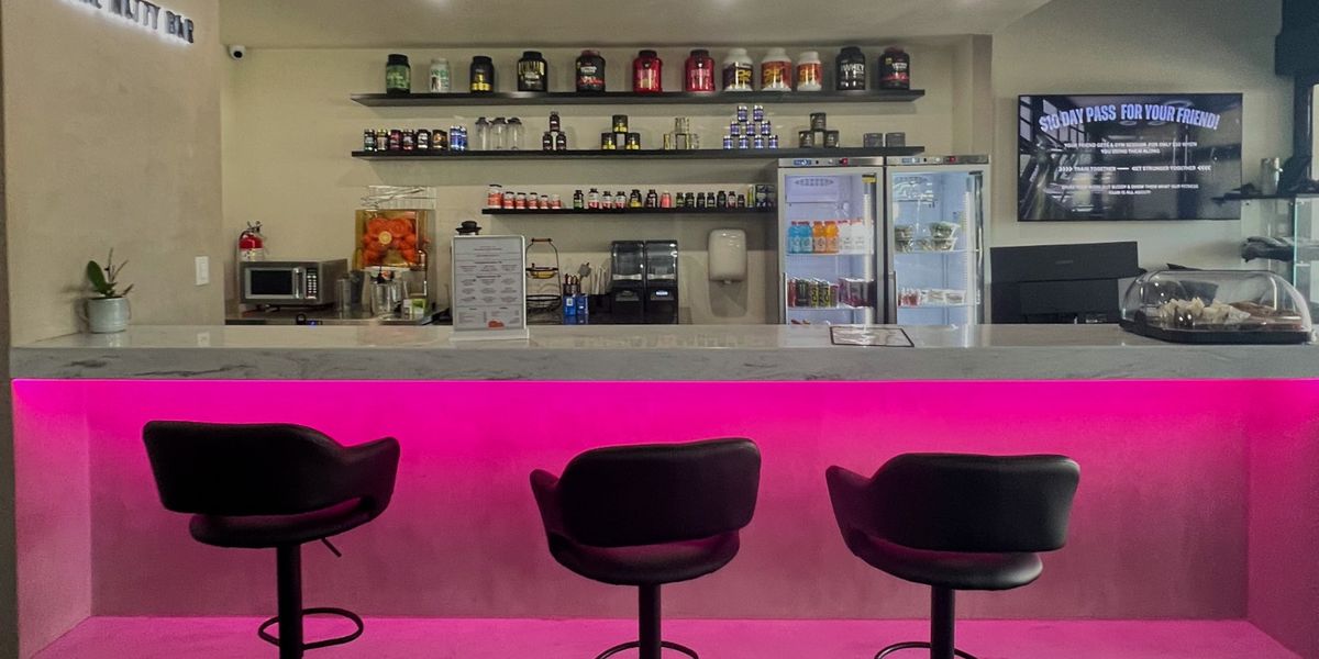 The smoothie bar at Solis Body Club with pink-lit counter, stools and protein shelves