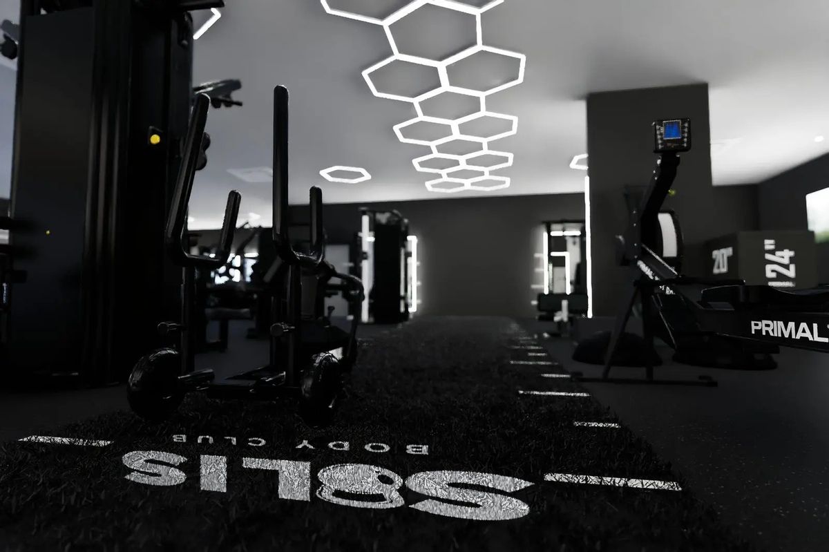 The Solis Body Club logo on the training turf, with a sled and a Primal rower