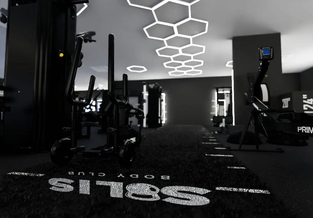 The Solis Body Club logo on the training turf, with a sled, a Primal rower and the hexagon lights